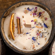 Coconut-shell candle with wooden wick, scented with cinnamon and orange, featured as the “Joy & Prosperity” aromatherapy candle.